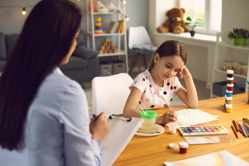 Child psychologist. A woman psychologist with a clipboard works with a little girl patient in a...