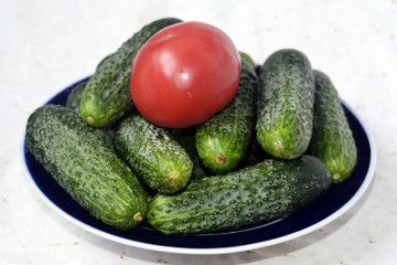 Red tomato on green cucumbers fresh vegetables close up