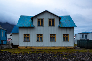 
landscape in the town of Ólafsfjörður, in the north of iceland. The typical house has a white facade and a blue roof. The sky is gray and cloudy