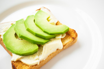 Sandwich with avocado slices, garlic and white sauce on toasted bread on a white plate close-up