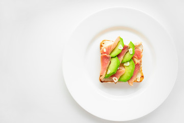 Sandwich with salmon, avocado, garlic and white sauce on toasted bread. The sandwich is on a white plate, on a white background.