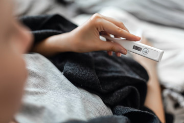 A woman is sick at home, checks the temperature with a thermometer. The thermometer indicates an...