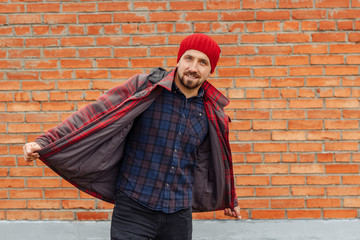 Naklejka premium Delighted man in red checkered jacket and trendy plaid shirt standing on background of brick wall