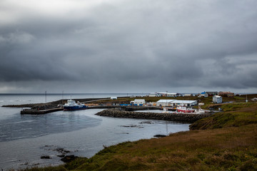 Fototapeta na wymiar landscape with the port of the island of grimsey in the north of iceland, off the arctic circle. The sky is loaded with clouds and a moored boat awaits tourists
