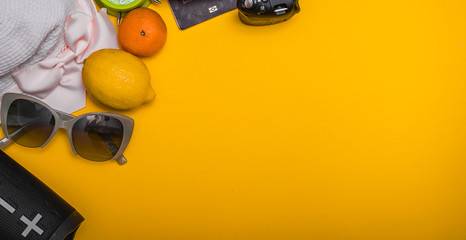 Beach cloth and accesories. Wireless speaker, fruits, sunglasses and camera on yellow background. Top view with copy space.