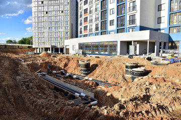 Laying heating pipes in trench at construction site. Installing concrete sewer wells and...