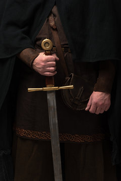 cropped view of medieval Scottish knight in mantel with sword