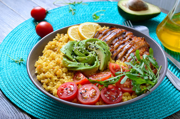 Bulgur with grilled chicken breast, fresh vegetables, avocado, arugula. Diet lunch on a wooden table. Healthy food