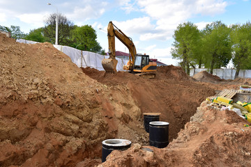 Excavator on earthwork during the laying of pipes of the heating system to a new residential building at the construction site. Laying concrete sewer wells, rings and manholes in ground.