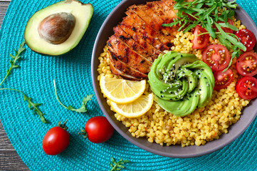 Bulgur with grilled chicken breast, fresh vegetables, avocado, arugula. Diet lunch on a wooden table. Healthy food. Top view.