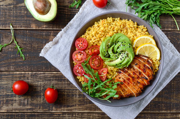 Bulgur with grilled chicken breast, fresh vegetables, avocado, arugula. Diet lunch on a wooden table. Healthy food. Top view.