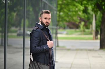 young serious man with beard standing next to building 