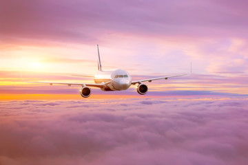 Passenger airplane in the morning sun flies high above the pink-tinted clouds with glare on the...