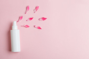 white plastic bottle of floral facial moisturizing toner or rose hair spray  and petals isolated on pastel pink background, flay layout, top view, natural organic beauty product