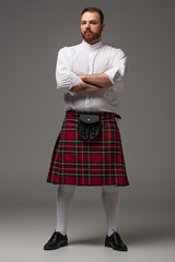 Scottish redhead man in red kilt with crossed arms on grey background
