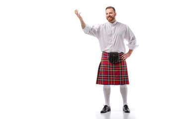 smiling Scottish redhead man in red kilt pointing with hand on white background