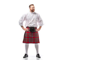 smiling Scottish redhead man in red kilt with hands on hips on white background