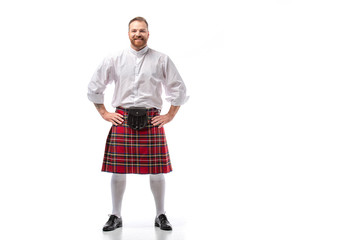 smiling Scottish redhead man in red kilt with hands on hips on white background - obrazy, fototapety, plakaty