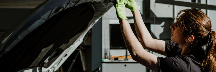 Female mechanic opening a car hood
