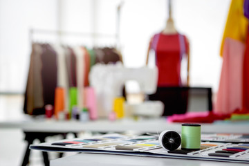 Fashion design studio and crafting tools in work shop, sewing accessory and tailor bobine de fil on table, colorful fabrics, hanging clothes, mannequins standing