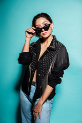 Beautiful woman portrait wearing a leather jacket and jeans with sunglasses on a blue background