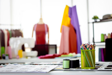 Fashion design studio and crafting tools in work shop, sewing accessory and tailor equipment, colored pencils in box, bobine de fil, colorful fabrics, hanging clothes, mannequins standing