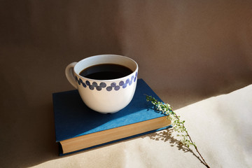 A mug of black coffee on a background of craft paper, next to a branch with white flowers