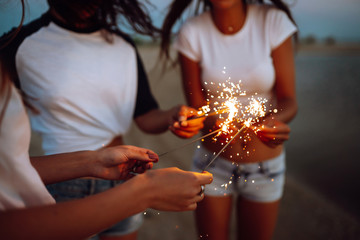 The sparklers in the hands of young girls on the beach. Three girls enjoying party on beach with sparklers. Summer holidays, vacation, relax and lifestyle concept.