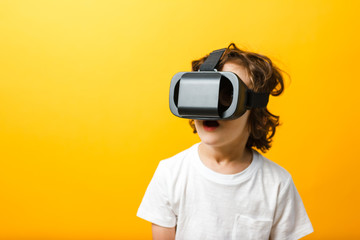 Fototapeta premium Close-up of little boy in virtual reality headset. Boy wearing virtual reality glasses white tshirt at yellow background