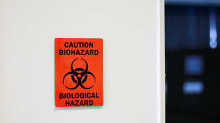 The Caution sign "Biological Hazard” for warning inflected biohazard area, a safety sign warning on white wall in laboratory room, useful for caution who working in microbiology medical science room.