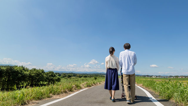 自然の中ベビーカーを押し散歩する若い夫婦の後ろ姿