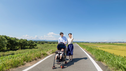 自然の中ベビーカーを押し散歩する若い夫婦(正面)