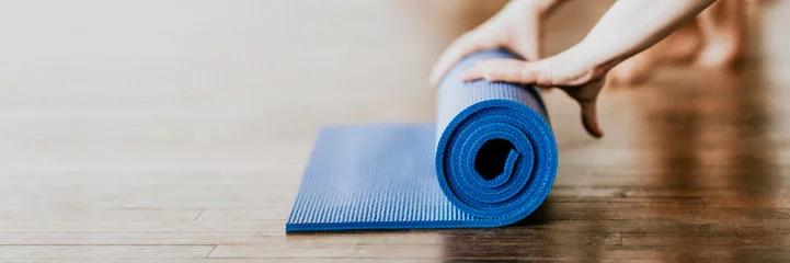 Foto auf Acrylglas Yogaschule Yogi rolling her blue yoga mat