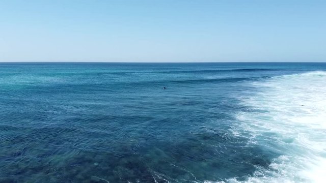 A surfer paddling out in between some waves at PontaPreta in CaboVerde, sunny weather (Drone shot)