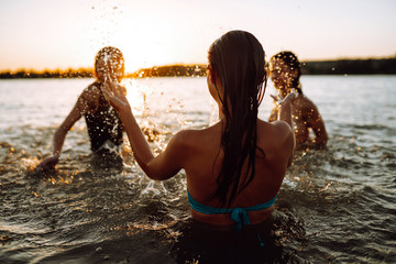 Three young girls  splashing water in the sea. Happy friends having fun in the waves on the beach at sunset time. Summer holidays, vacation, relax and lifestyle concept.