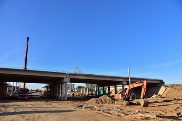 Excavator working at construction highway ramps and bridgeworks. Roundabout and traffic bridge construction. Road work on traffic highway, road intersection junction and freeway. Bridge project works