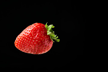Front view of a red strawberry stuck in a knife isolated on a black background.