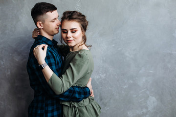 Handsome guy hugs his girlfriend. Happy Cheerful Family. Posing against a gray wall. Hugging.