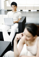 Woman talking on the mobile phone with man using laptop in the background