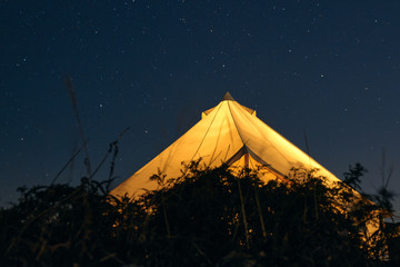 Glamping illuminated from the inside against a starry sky on a summer night. Camping and outdoor concept.