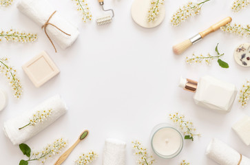 Fototapeta na wymiar Stylish White Spa concept. Flowering branches of bird cherry on white baground. White candle, soap, cream, towels. Copy space. Flat lay. 