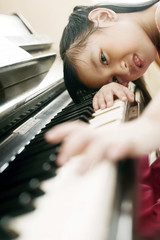 Girl playing piano while resting her head on her hand © ImageHit