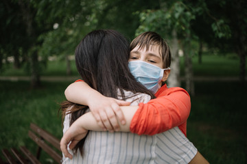 Naklejka premium Back of brunette woman hugging little girl with antivirus mask. Portrait of mother and daughter cuddling in park during coronavirus pandemic