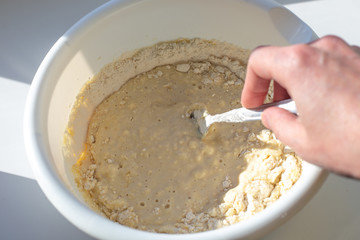 kneading a batter of flour and milk in a white bowl with a fork, preparing delicious pastries