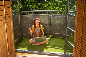A young adult woman on video call at a laptop on her balcony in London during covid-19 lockdown