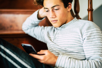 Bored handsome male teeanger at home use cellular phone and internet connection to read new or chat with friends - concept of coronavirus lockdown worldwide quarantine emergency
