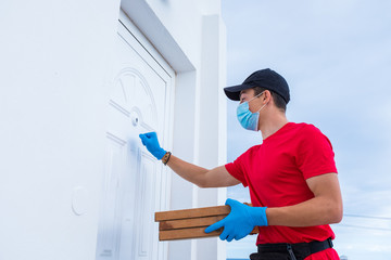 pizza man knocking at the door of a house wearing medical and surgical mask to prevent the infection giving pizza - food delivery at their addres in the middle of pandemic