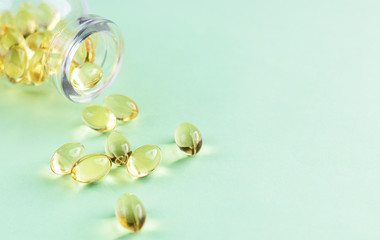 Yellow omega-3 capsules from a glass bottle on a green background. Copyspace for text. Health care, natural, natural supplements. Lifestyle concept