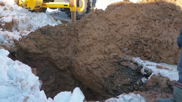 From above dirty bucket of modern loader digging hole in wet earth near snow on winter day