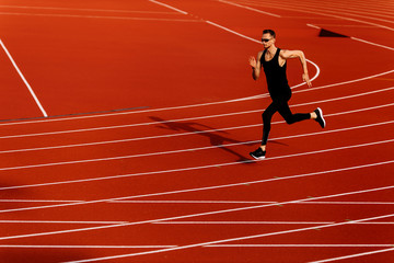 Young athlete man runs around the stadium dressed in a black sportswear 